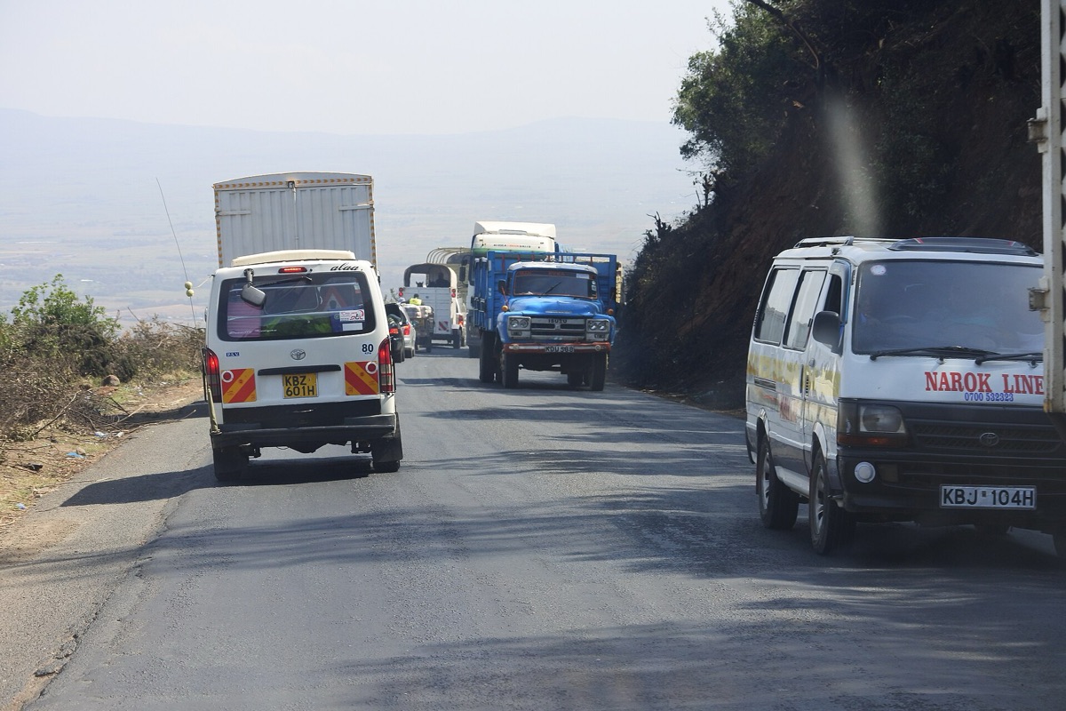 A minibus drives away on the left of a two-lane Kenyan road as a white van and a blue lorry come the other way
