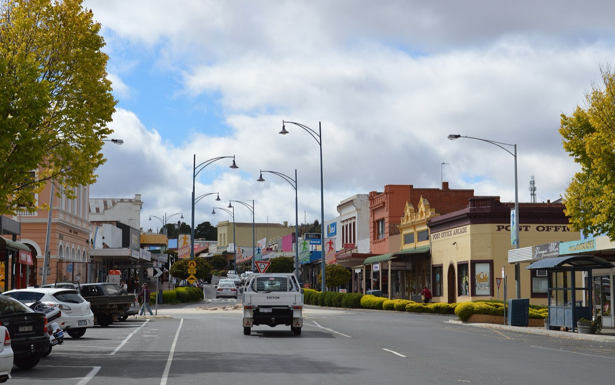 An Australian country main street with Post Office and Pharmacy signs and a white ute driving away from the camera