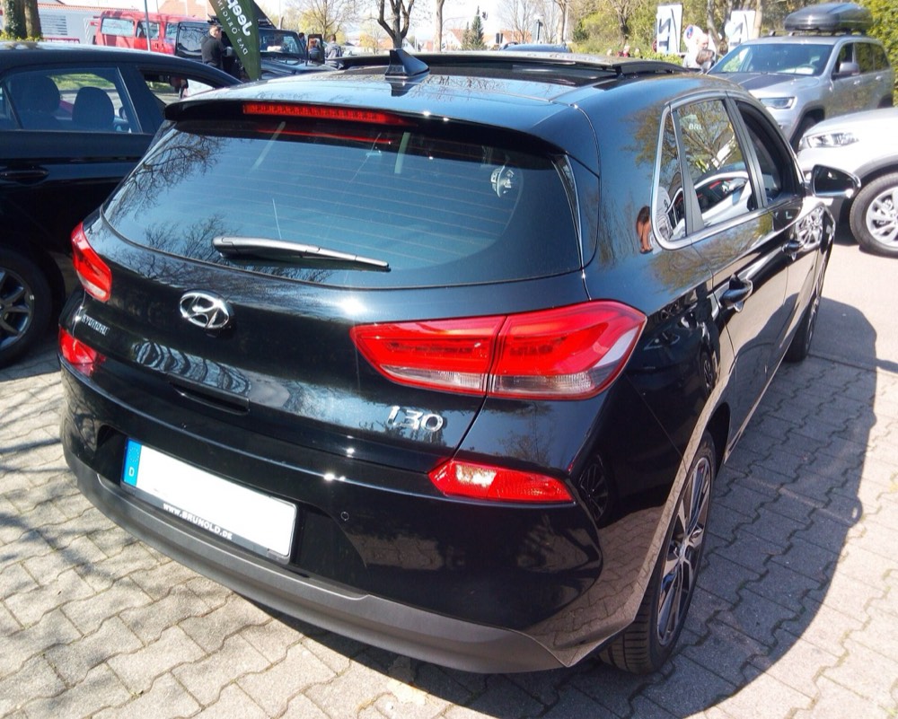The rear of a black hatchback showing a blank number plate with a blue band and the letter D