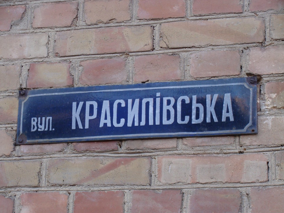 Blue enamel street plate bolted to a brick wall, reading vul. Krasylivska in white Cyrillic capitals
