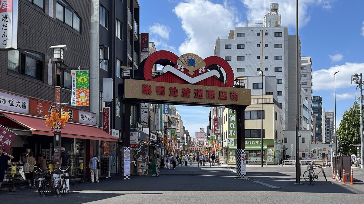 Tokyo shopping street gate with a red kanji sign, shop fascias carrying kanji and hiragana on the left, blue sky
