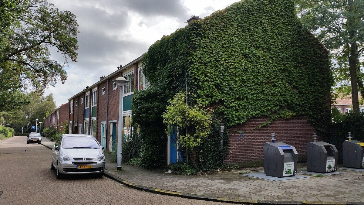 A quiet Dutch residential street with a silver car parked by the kerb showing a yellow front number plate