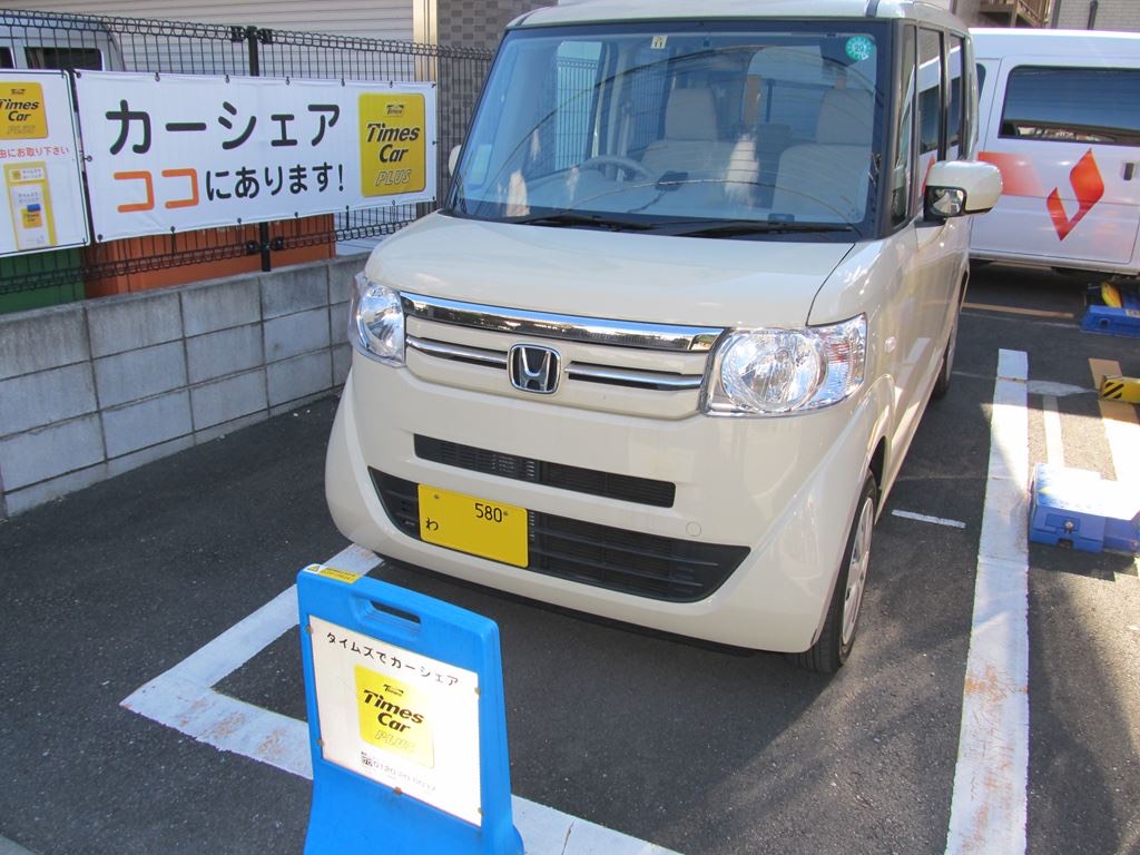 A cream-coloured Japanese kei car parked in a car-share bay, its front number plate yellow with black characters