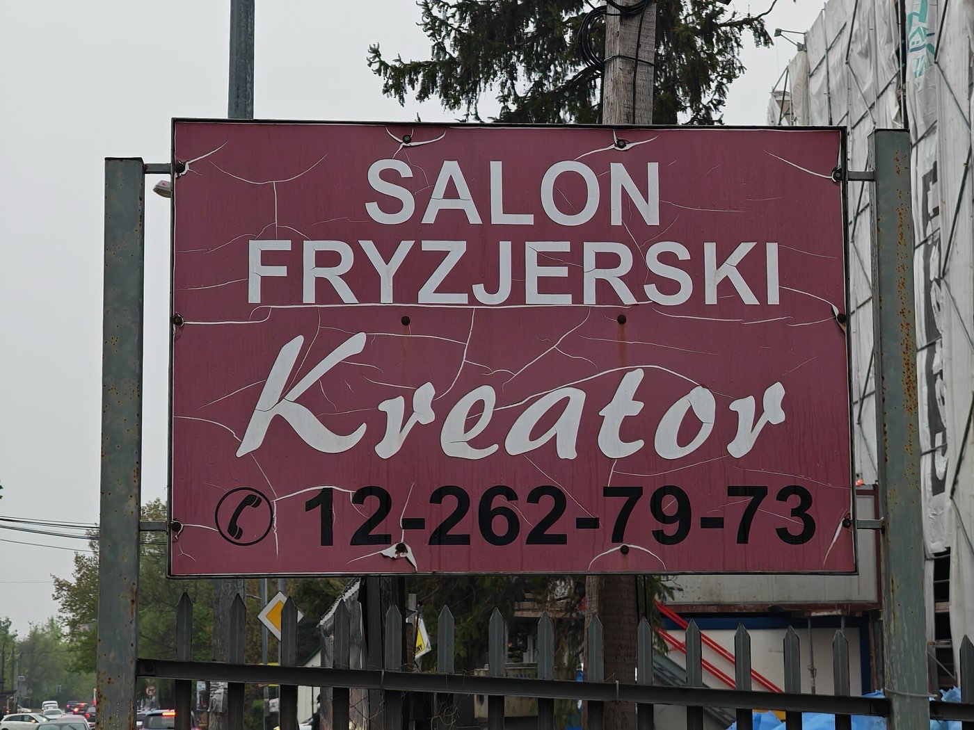 Verwittertes kastanienbraunes Schild mit SALON FRYZJERSKI Kreator und der Telefonnummer 12-262-79-73 darunter