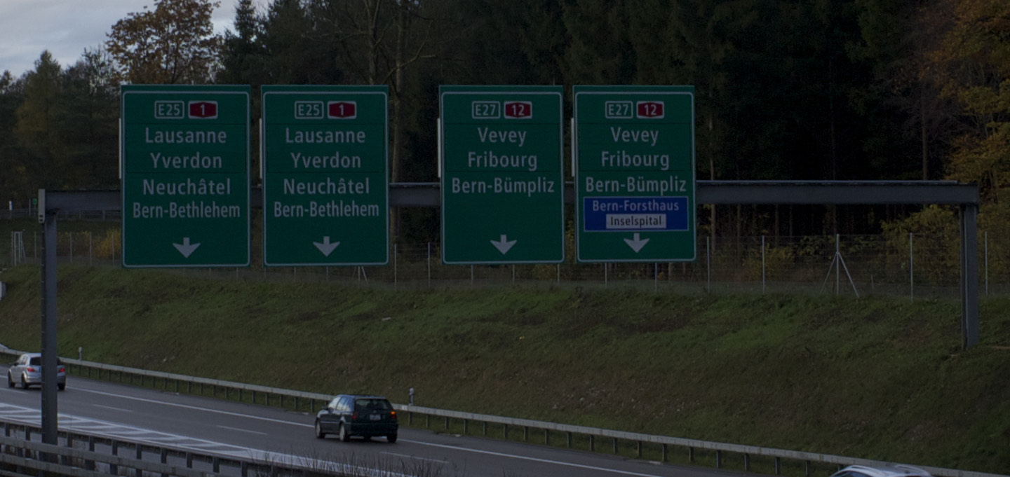 Quattro cartelli autostradali verdi con numeri di strada rossi e un piccolo pannello blu, su un'autostrada vicino a Berna