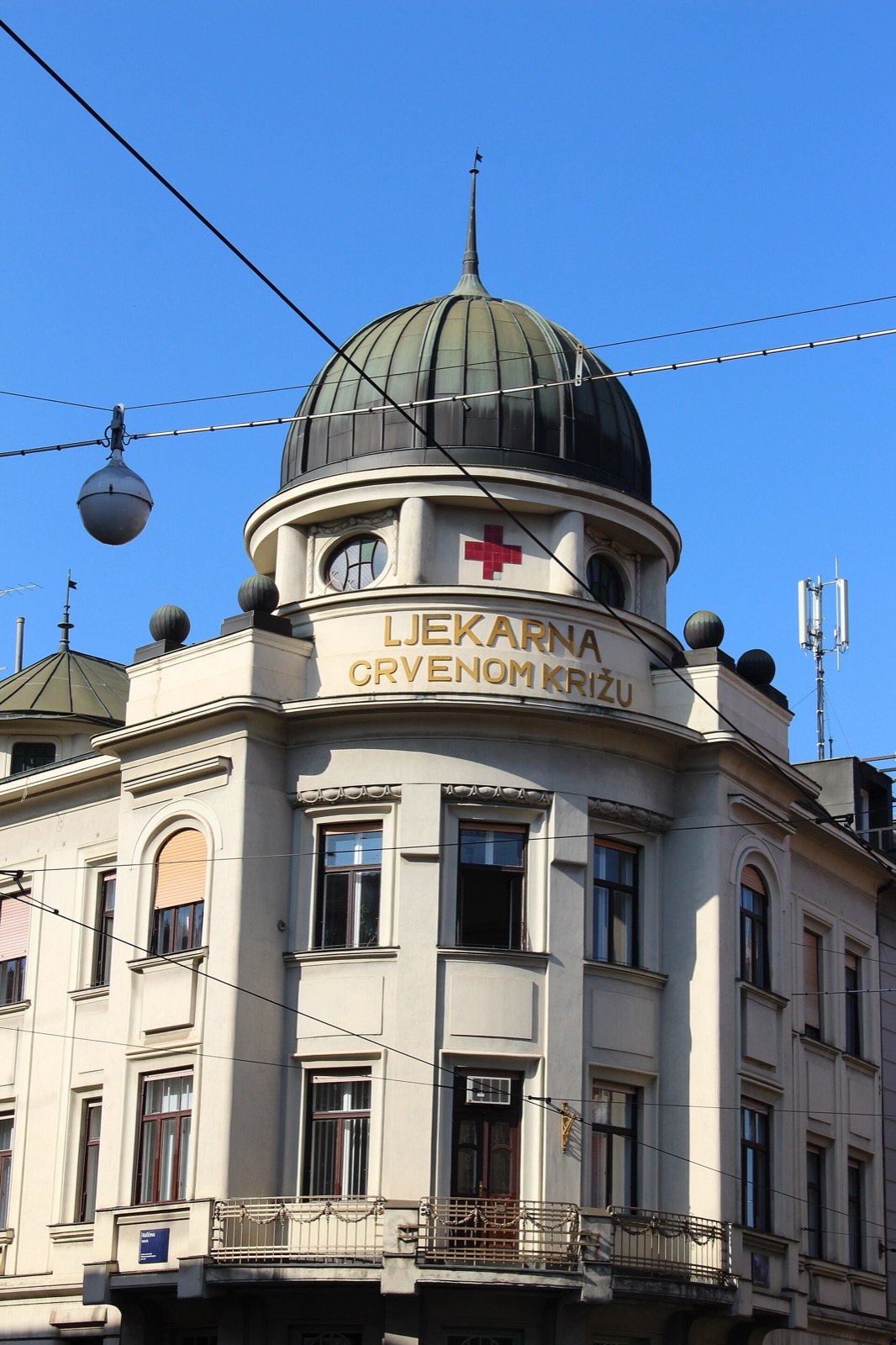 A domed corner building with large gold letters reading LJEKARNA under a red cross
