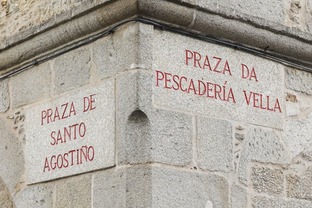 Two carved granite street signs on a stone corner reading Praza de Santo Agostiño and Praza da Pescadería Vella