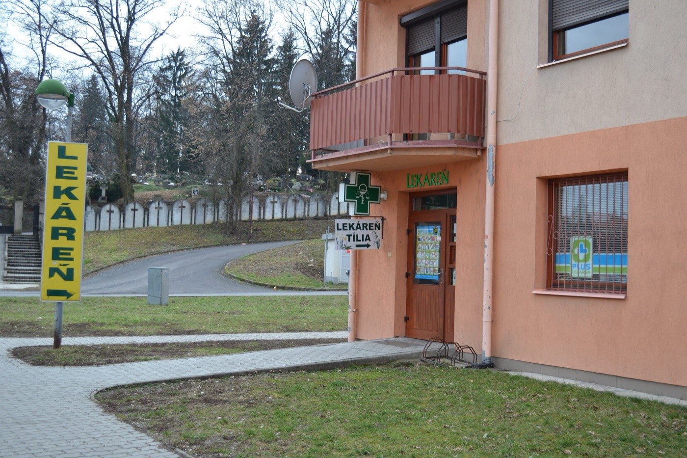 A yellow pole sign spelling LEKÁREŇ vertically, beside a building with a green cross and another LEKÁREŇ sign